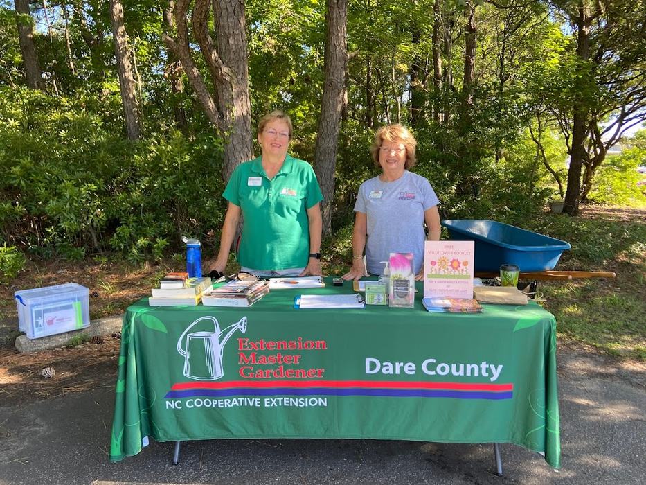Two people behind a table with "Extension Master Gardener Dare County" tablecloth and brochures