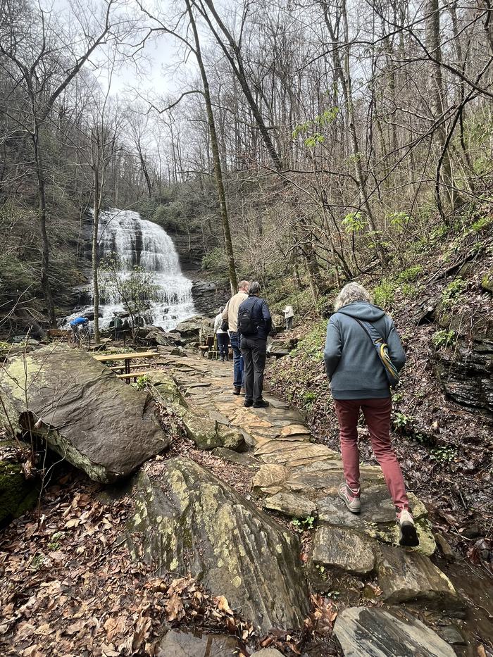 Hikers move toward a large waterfall in the distance.