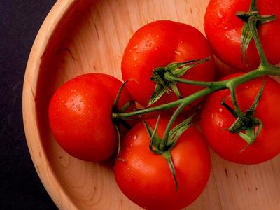 Vine of five red tomatoes with water droplets in a wooden bowl