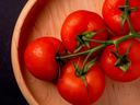 Vine of five red tomatoes with water droplets in a wooden bowl
