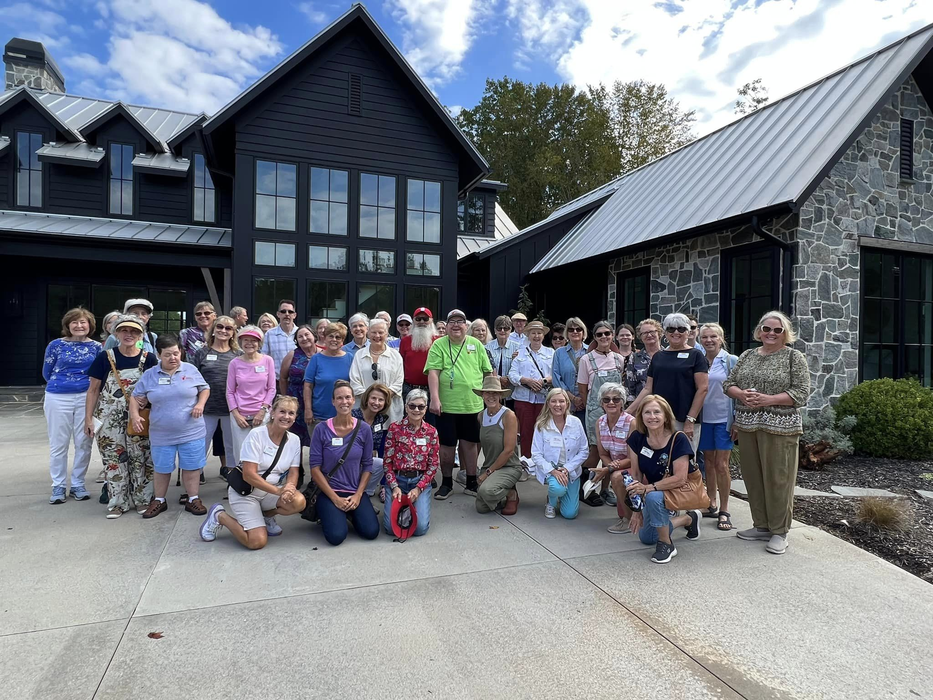 Large group of adults posing in front of a modern dark house with a stone wing