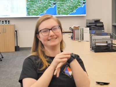 Person with glasses smiling at desk, checking a smartwatch in operations office (text: OPERATIONS)