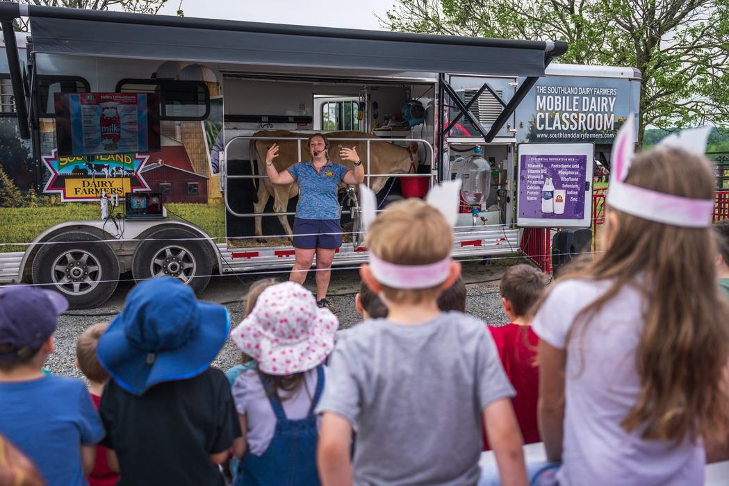 Instructor speaking to children in front of mobile dairy classroom with a cow.