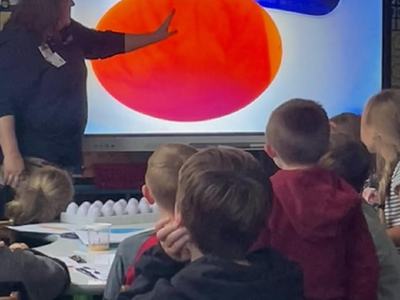 Teacher points to large orange circle on classroom screen while students watch