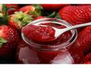 Jar of strawberry jam with a spoonful above the jar and whole strawberries around