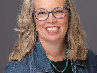 Woman with glasses, denim jacket, and turquoise necklaces, head-and-shoulders view
