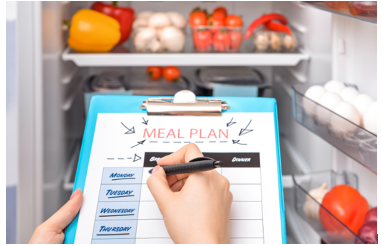 A person creates a meal plan in front of a full refrigerator