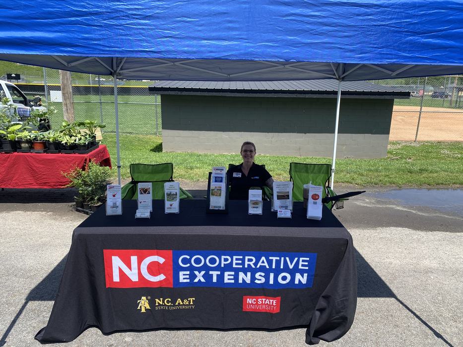 Outdoor booth under blue tent with NC Cooperative Extension tablecloth and brochures