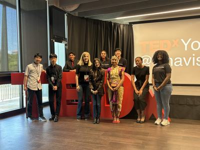 Group of presenters posing in front of large red "TEDx" letters and stage backdrop