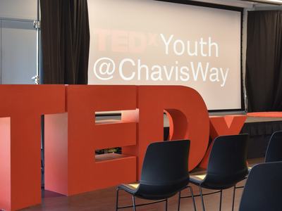 TEDx letters in a large room with a large screen in the background.