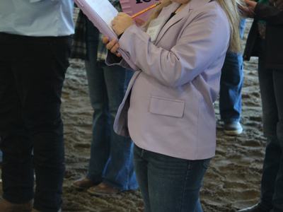 Young girl in lavender blazer writing on a clipboard while standing among peers