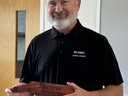 Gentleman in a black polo with NC State logo holds an award made of wood and shaped like North Carolina. 