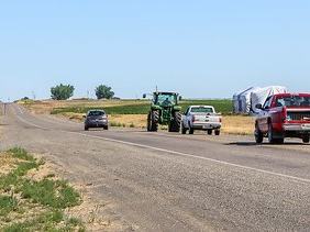 Cars riding behind a tractor on a road.