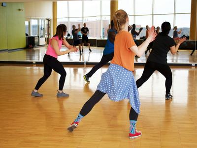People following an instructor in a mirrored dance studio, mid-step and clapping