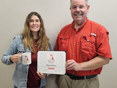 Two people holding a "Pride of the Wolfpack" certificate reading "Marcia Berry" and a mug
