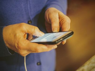 Senior citizens benefit tremendously from digital literacy! Picture shows a pair of hands belonging to a senior citizen holding and using an iPhone while it is charging. Photo by Joshua Hoehne on Unsplash