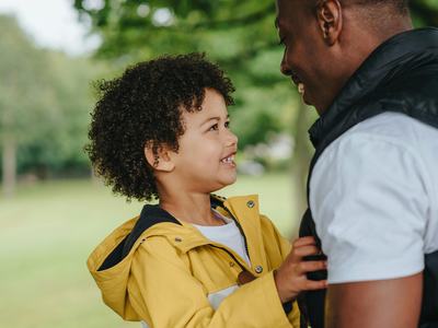 Child in yellow raincoat looking up and holding an adult's vest outdoors