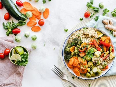 bowl of quinoa and vegetables on table with vegetables scattered around it