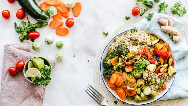 bowl of quinoa and vegetables on table with vegetables scattered around it