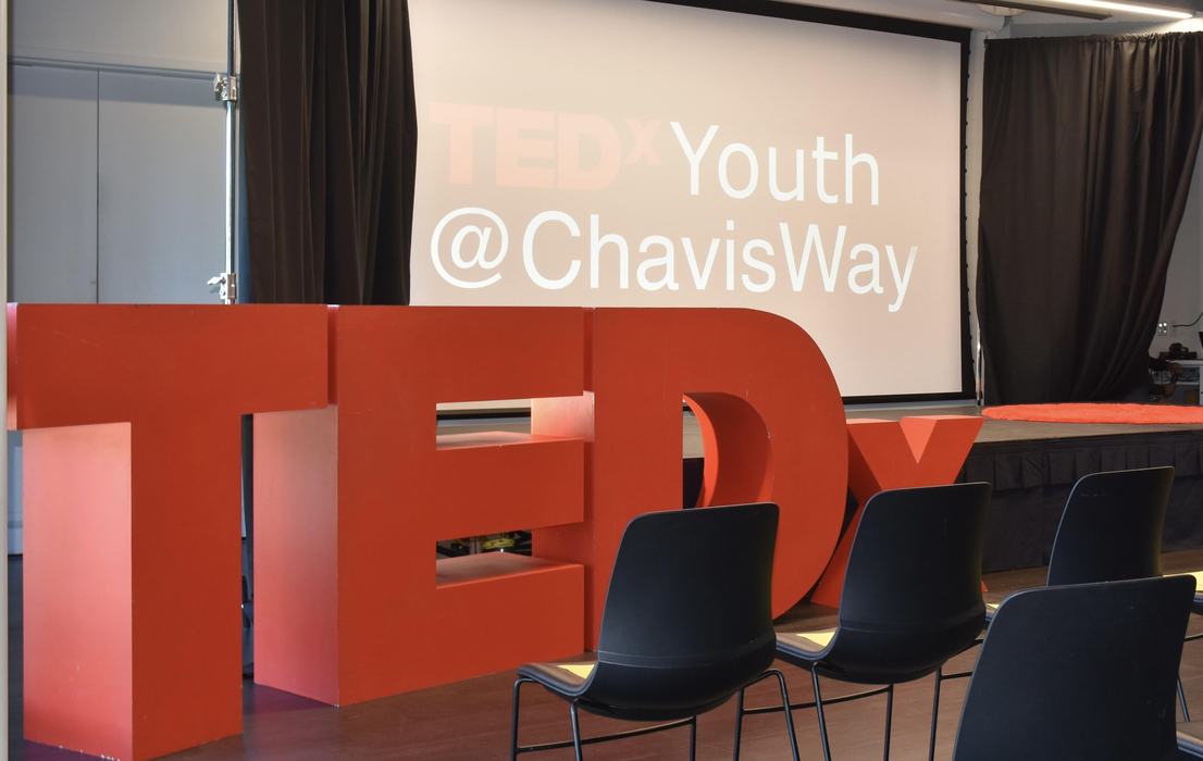 Bright red TEDx letters in front of a large screen. 