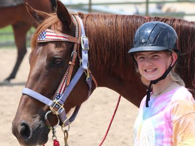 Young girl in riding helmet leads brown horse on a red lead rope in an outdoor arena