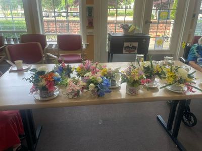 Table with six floral centerpieces in teacups arranged on a long table by windows