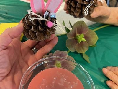 Two pinecone bunny crafts with felt ears and googly eyes held over a pink drink