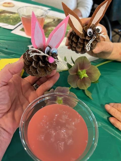 Two pinecone bunny crafts with felt ears and googly eyes held over a pink drink