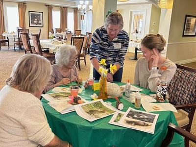 Four women seated around table doing crafts with papers, glue, and daffodils.