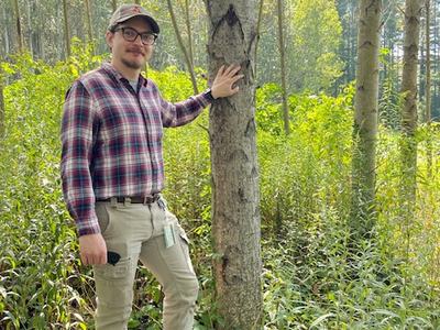 Image of Dr. Will Kohlway standing next to a poplar tree in a forest.