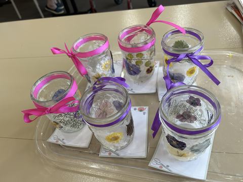 Six glass jars decorated with pressed flowers and pink/purple ribbon bows on a tray