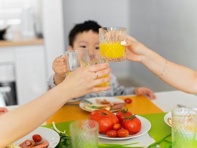 young child holding up glass to two adult hands also holding up glasses at table