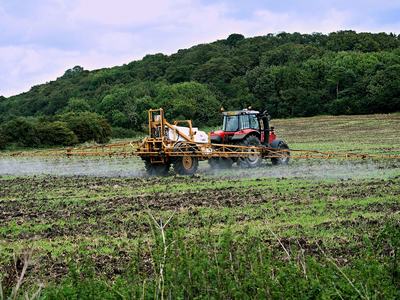 Tractor with boom sprayer spraying a field near wooded hillside