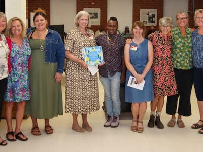 Group of nine people standing indoors, one person holding a blue award plaque
