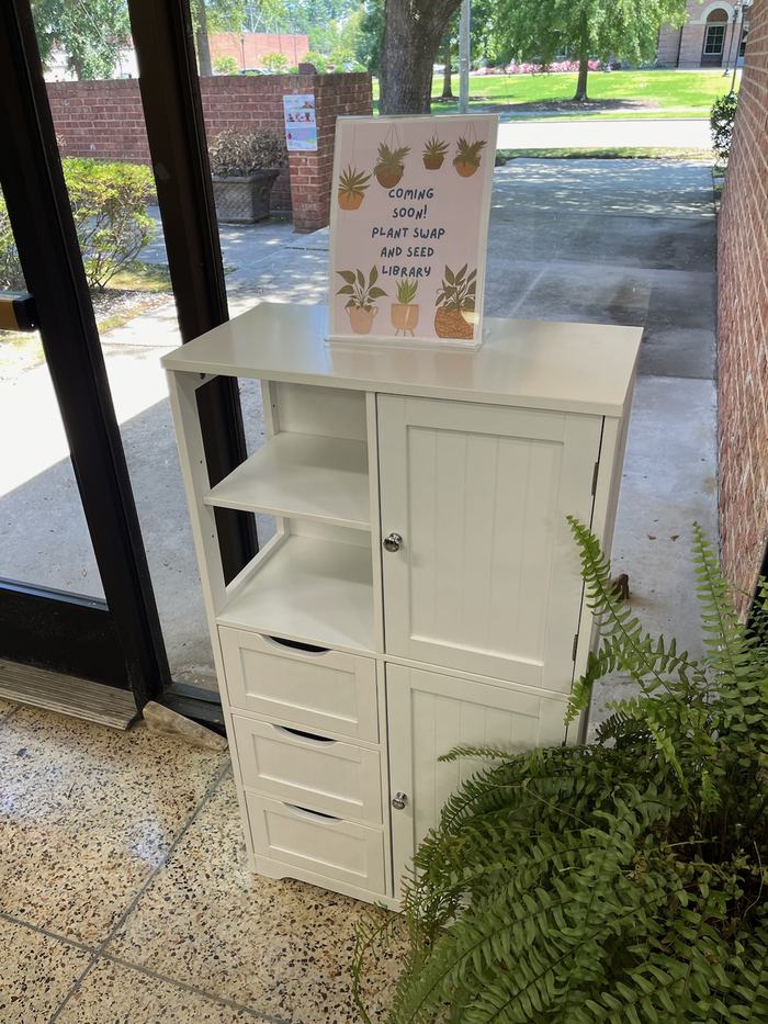 A white cabinet that displays a sign reading "Coming Soon! Plant Swap and Seed Library."