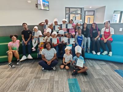 Group of children and adults holding certificates and wearing chef hats in a seating area