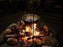 Cast-iron pot suspended over fire in a stone fire pit with burning logs