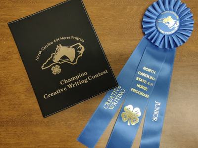 Black Champion Creative Writing Contest folder and blue North Carolina 4-H Horse junior ribbon