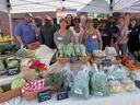 Farmers market stall displaying vegetables and packaged greens with vendors under a tent