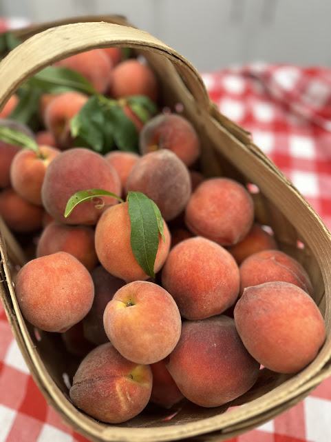 Basket of ripe peaches with leaves on red-and-white checkered tablecloth