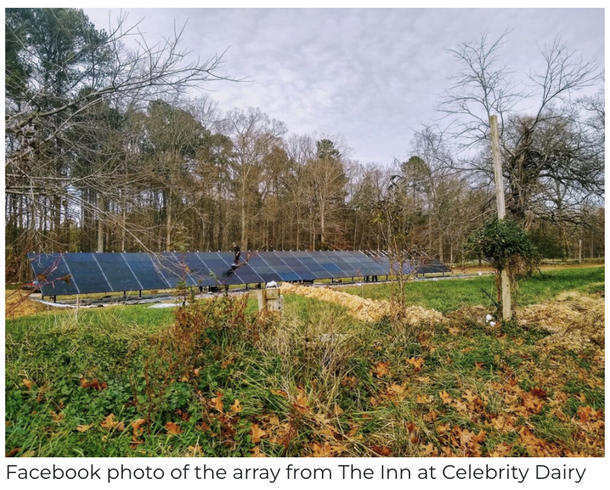 Ground-mounted solar panel array in a grassy field with leafless trees