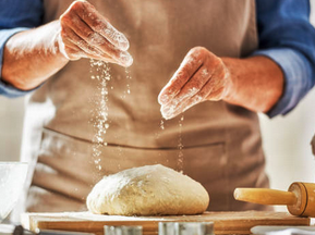 Hands sprinkling flour over dough on a work surface with rolling pin nearby