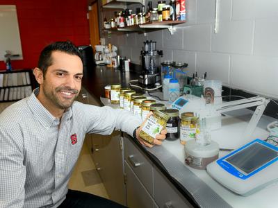 Man holding a labeled jar beside a row of jars and laboratory equipment on a countertop