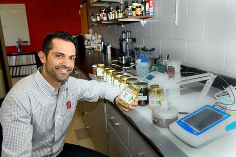 Man holding a labeled jar beside a row of jars and laboratory equipment on a countertop