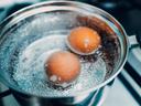 Saucepan stainless steel with boiling eggs breakfast in a water on a gas stove top view.