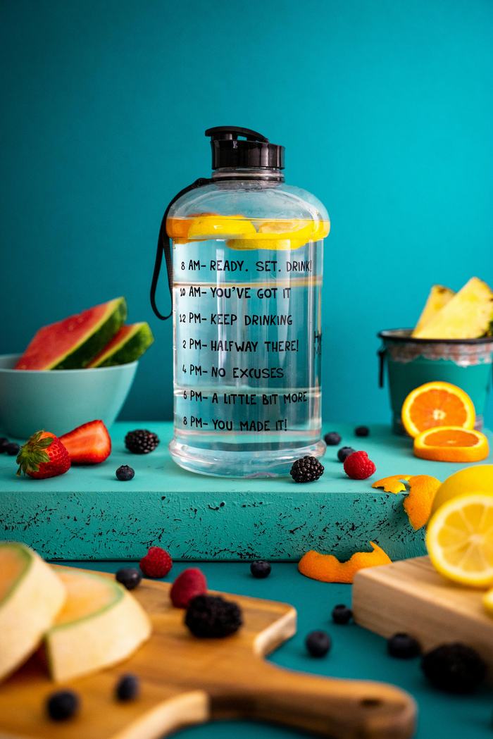 water bottle marked with motivation to hydrate and surrounded by various fruits on a blue background