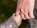 Adult hand holding a child's hand by the thumb, child wearing a jacket cuff