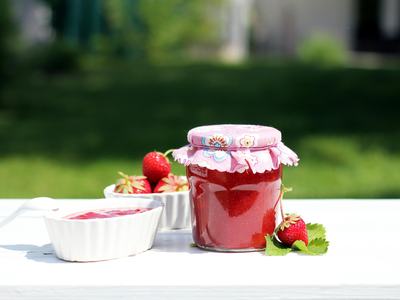strawberry jam surrounded by fresh strawberries in white bowl and on table