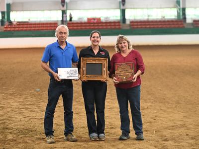 Three people standing in an indoor arena holding plaques reading "2024 North Carolina"