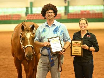 Man with plaque and blue ribbon beside horse; woman holding plaque reading "Champion 4‑H Alumni"